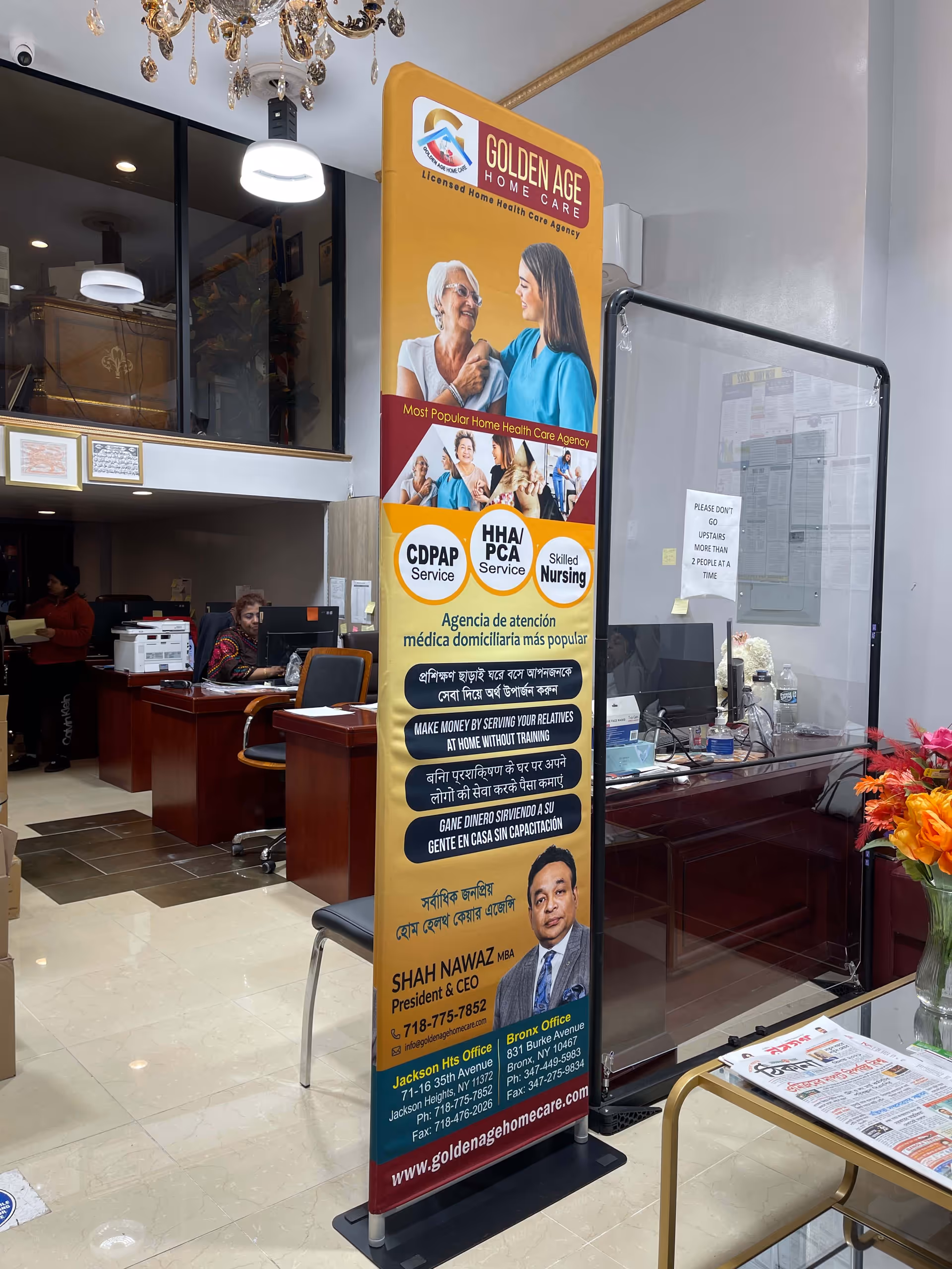 Tall Golden Age Home Care banner stands in a bright interior reception area with desks.
