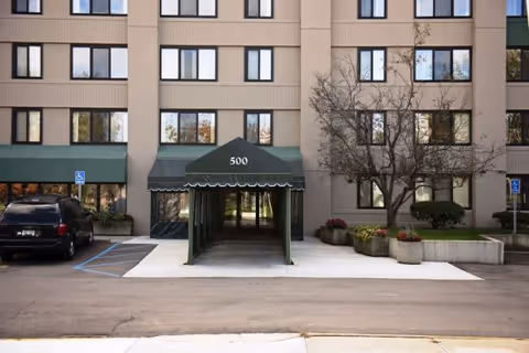 Exterior view of Wellspring Meadows Assisted Living entrance with a green awning and planters.