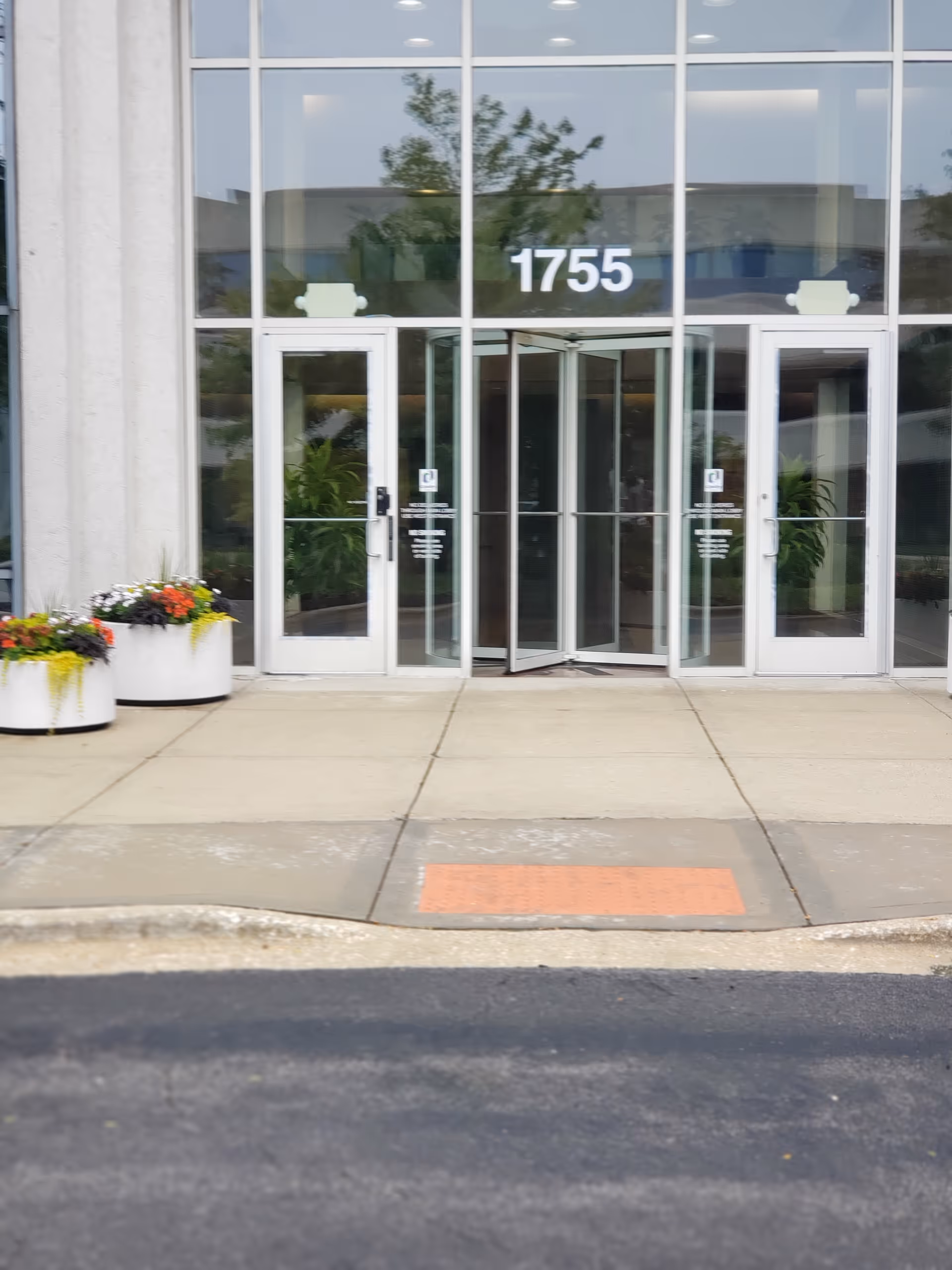 Glass-front entrance with large doors, address 1755, and planters with flowers.