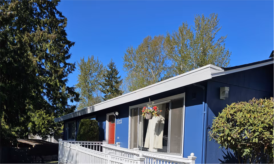 Blue single-story home with red door, white railing, and hanging flower basket on front porch.