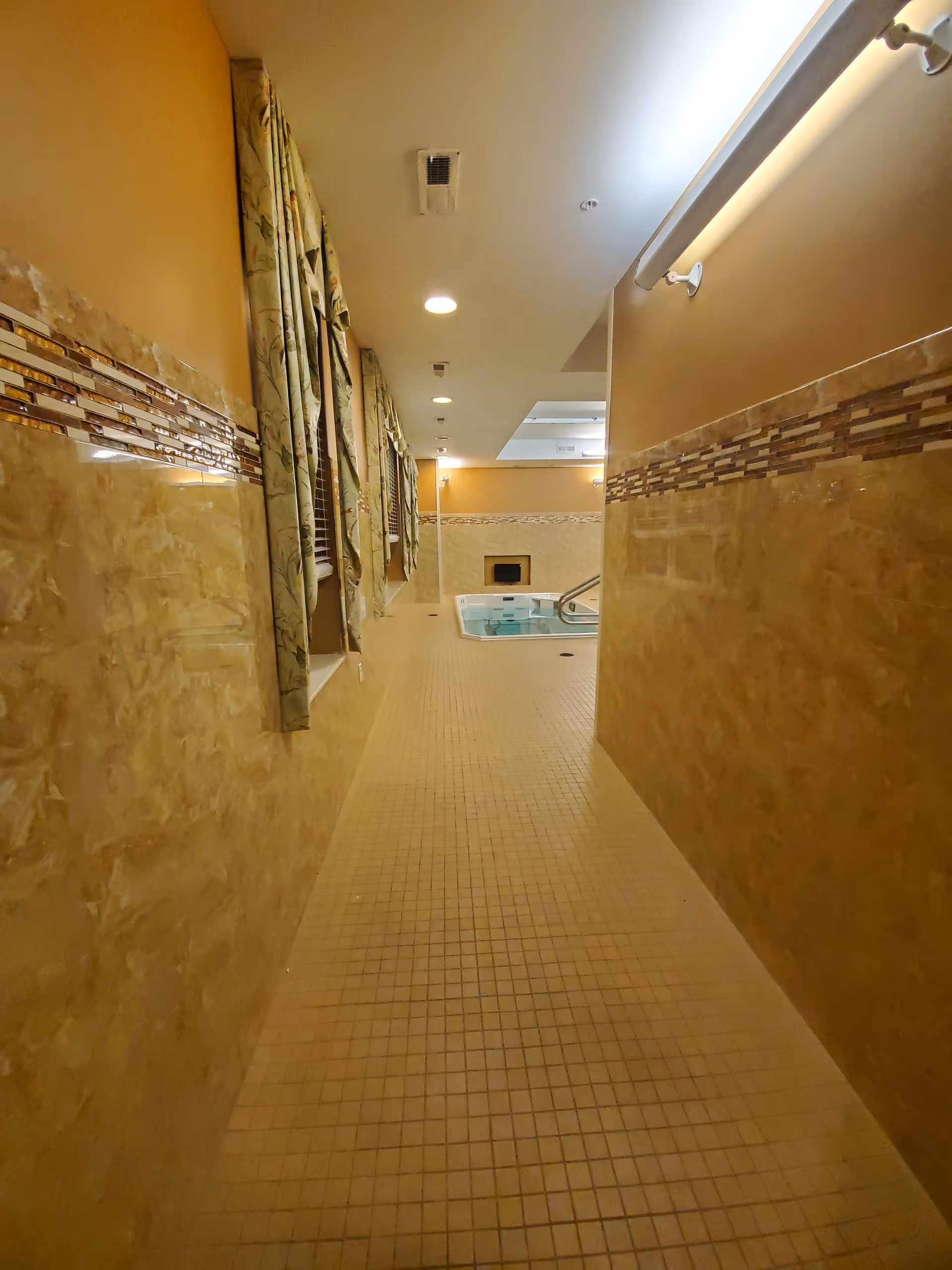 Narrow beige-tiled hallway leads to an indoor pool area at the end.
