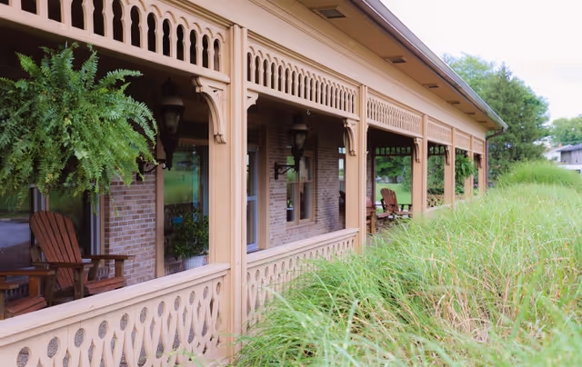 Exterior of a nursing center with a long covered porch and wooden chairs.