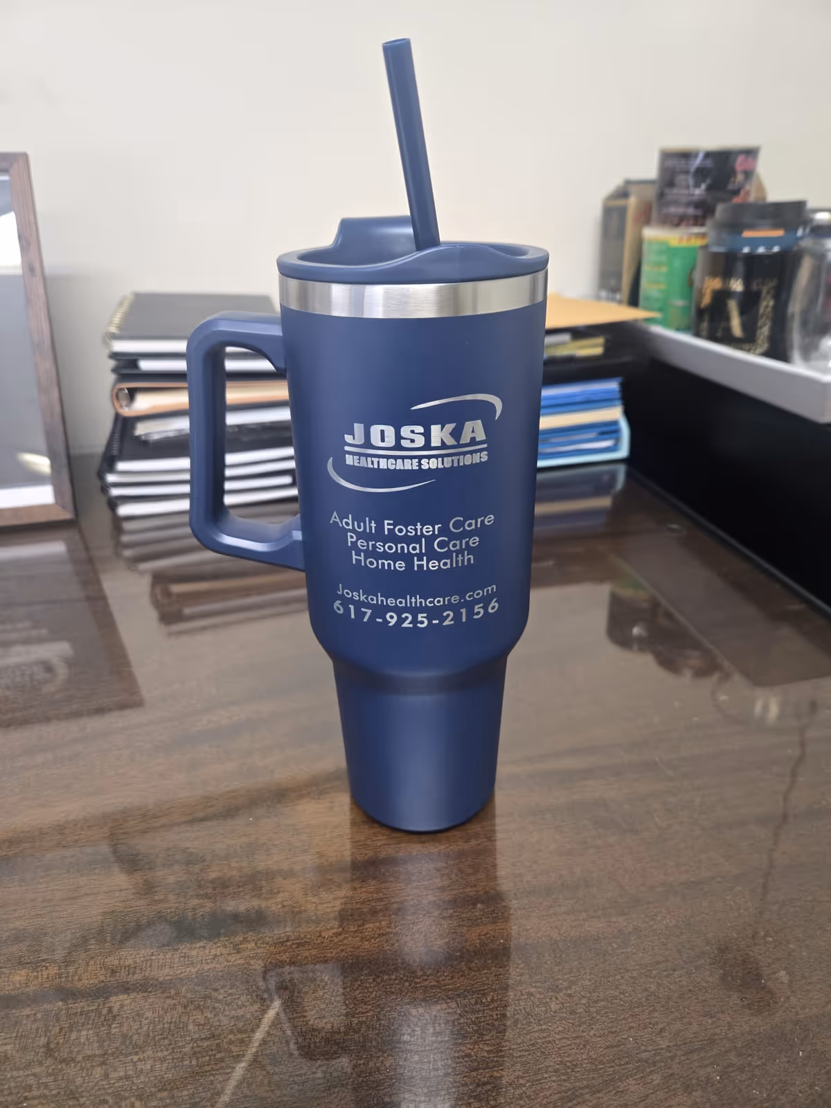 Blue Joska tumbler with straw sits on a wooden desk in an office