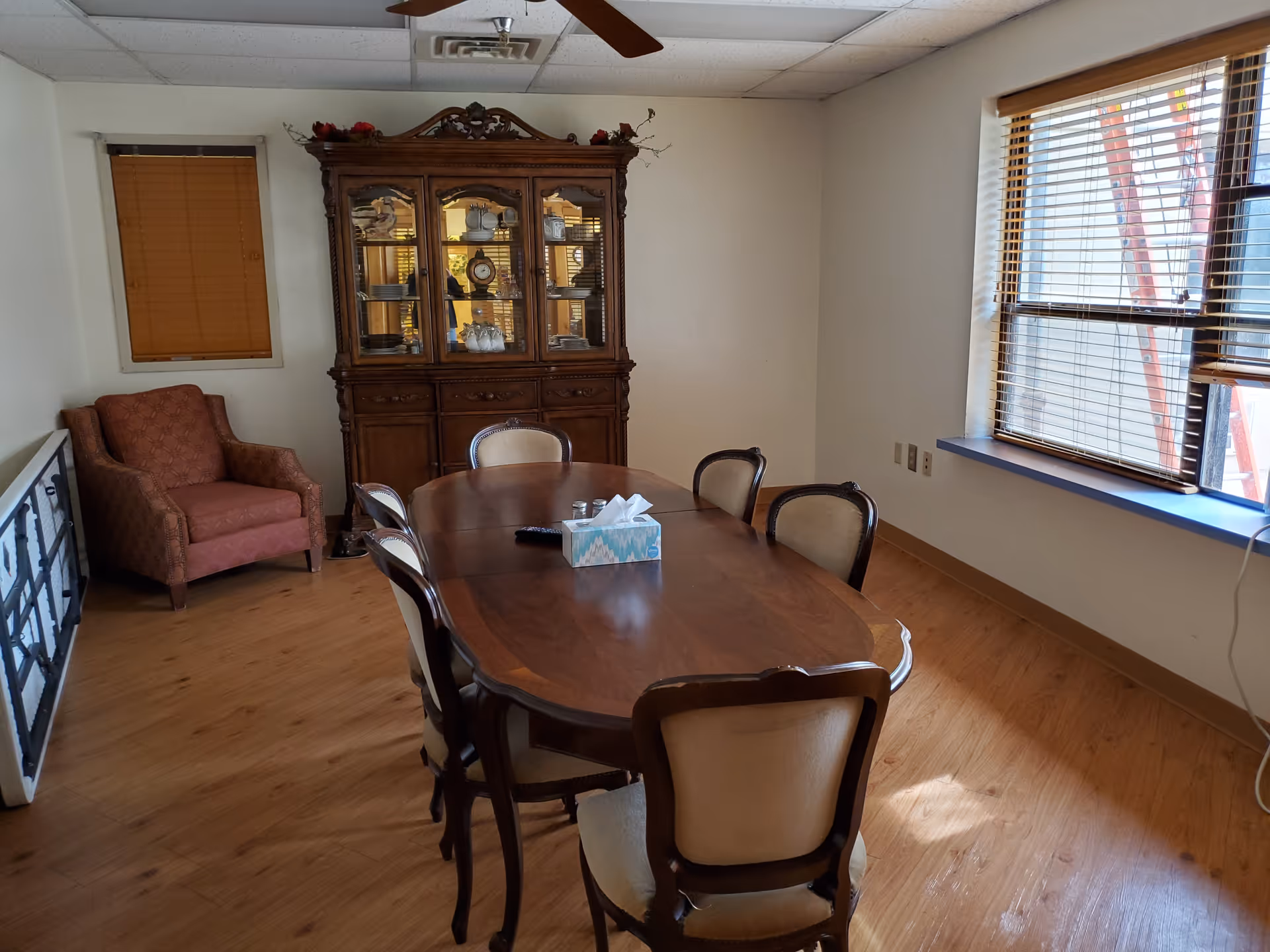 Wooden dining table with chairs in a room featuring a china cabinet and windows.