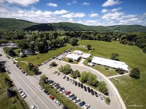 Aerial view of a senior living campus with a curved driveway, parking, and green fields.