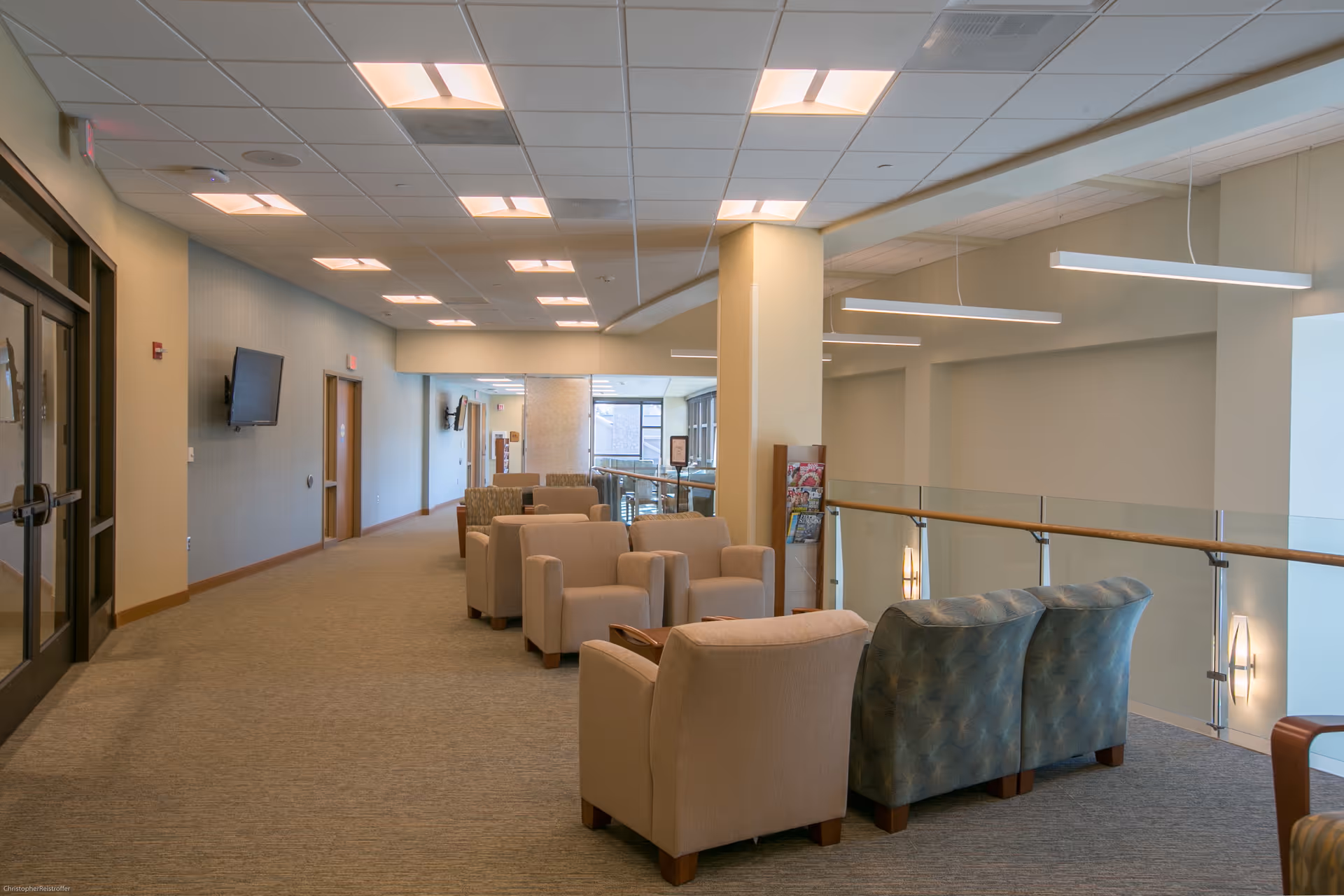 Bright senior living lounge with beige and blue chairs and glass railing.