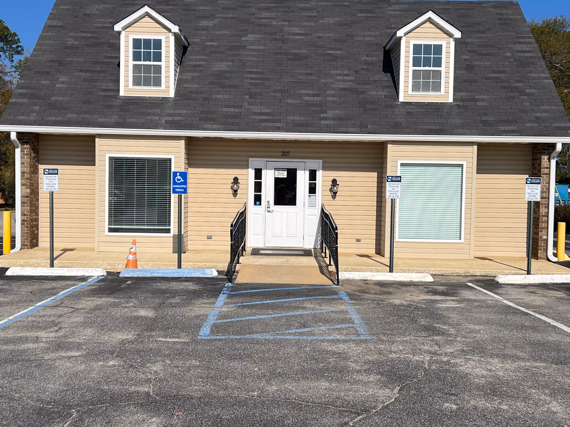 Front view of a beige two-story building with a wheelchair-accessible entrance and parking.