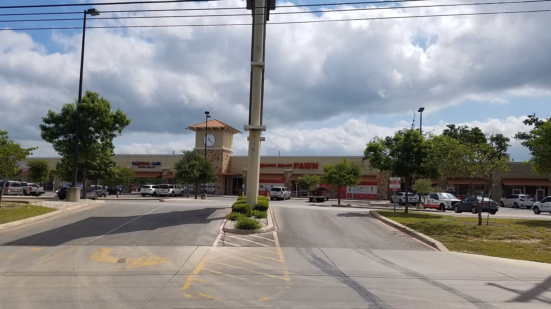 Exterior view of a strip mall with a clock tower and parked cars.