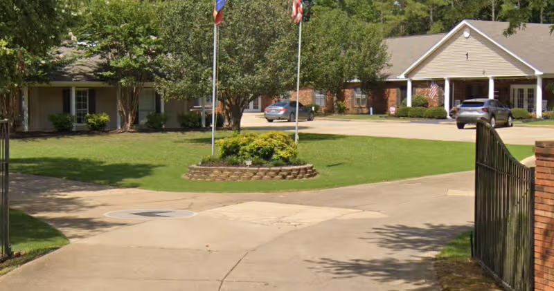 Front view of Creekside Manor Assisted Living with driveway, lawn, and flagpoles.