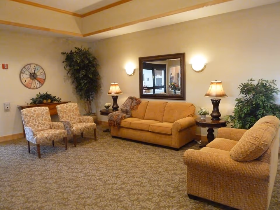 Comfortable seating area with sofas, armchairs, side tables, lamps, plants, and a wall mirror in a lounge.