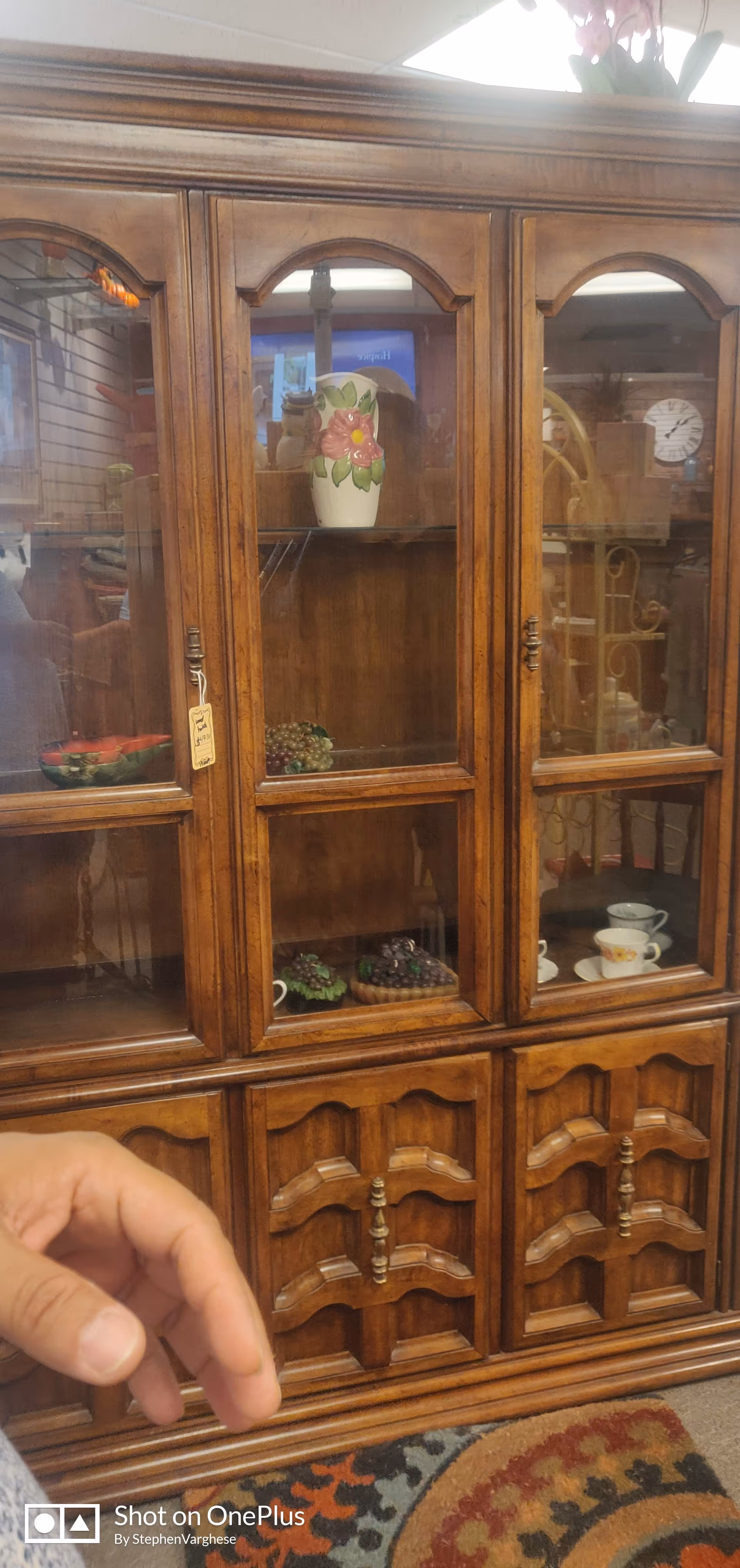 Wooden china cabinet with glass doors displaying vases and dishes, hand visible in foreground.