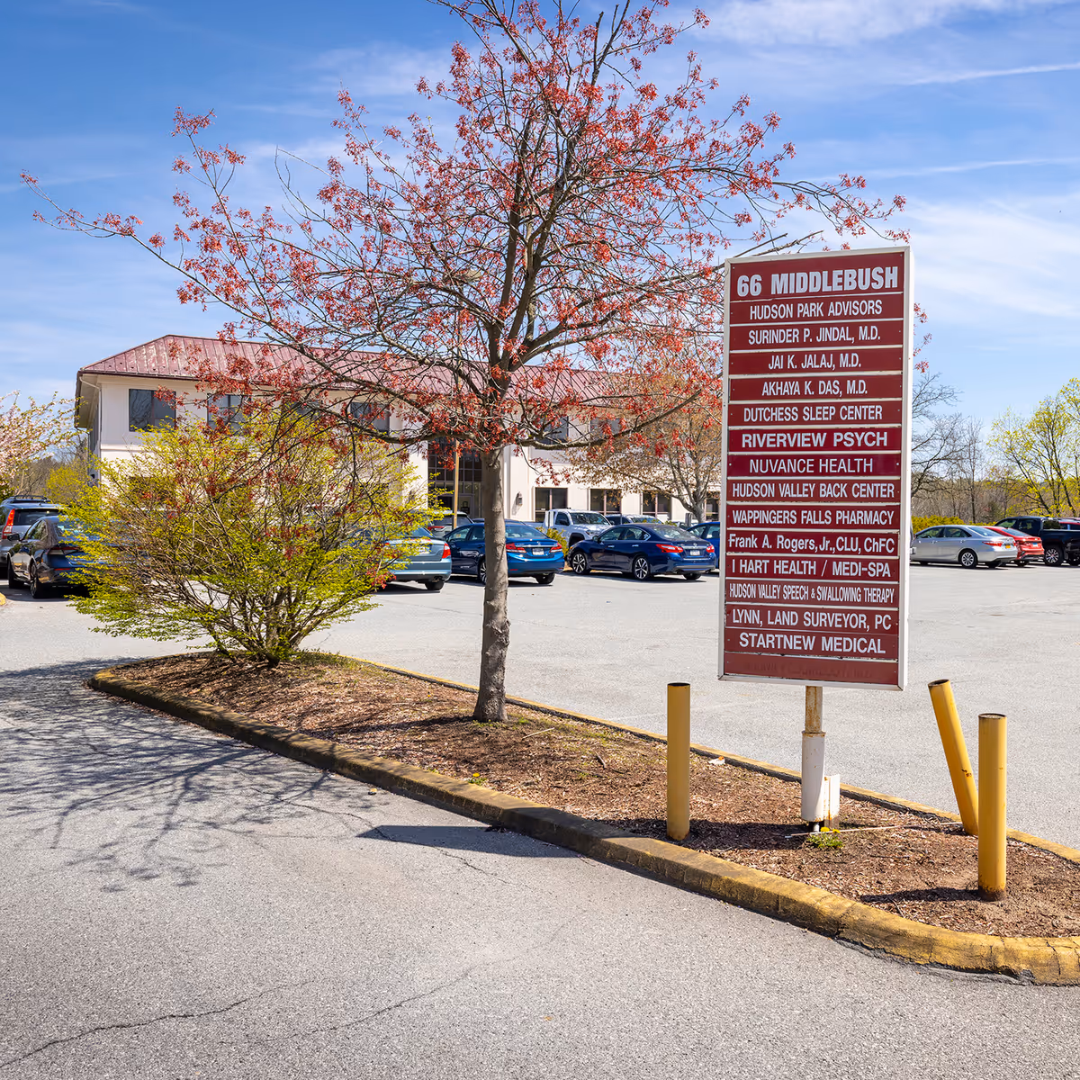 Exterior view of a medical practice building with a tall sign and parked cars.