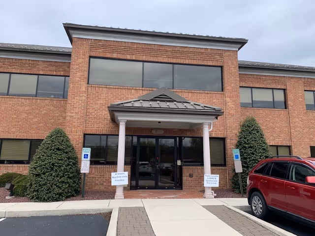 Hospice of Central PA entrance: brick building, columns, glass doors, shrubs, and a red SUV.