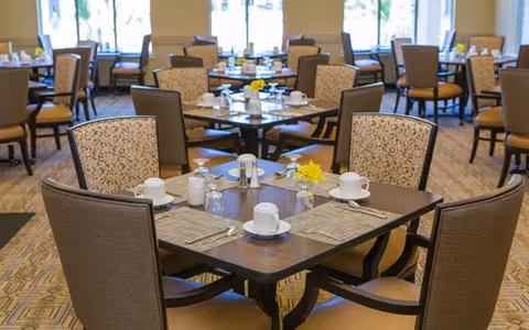 Dining room at Oasis at Scholars Landing with tables set for meals and yellow flowers.