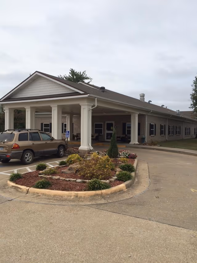 Front view of a senior living facility with columns, a driveway, and landscaped island.