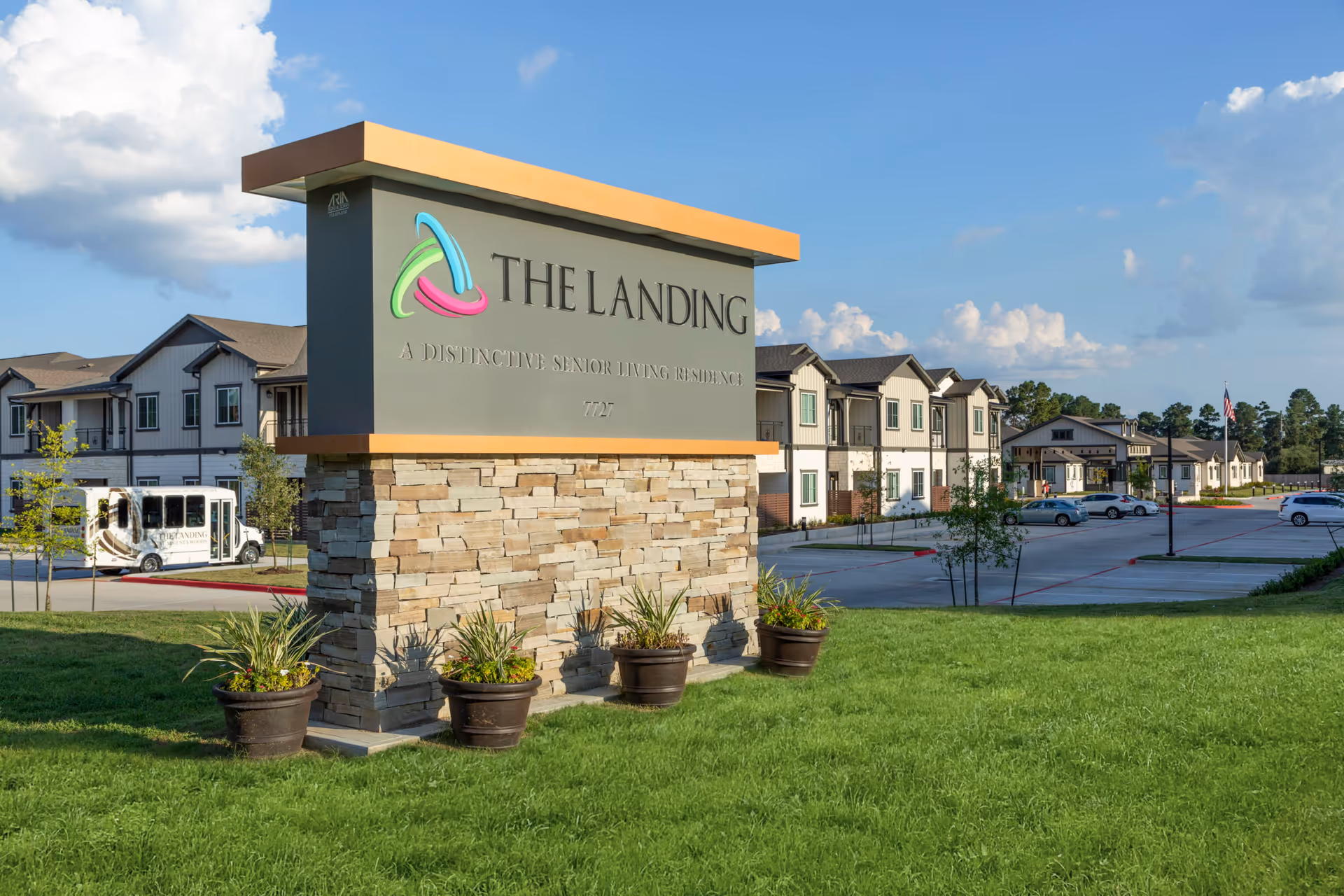Outdoor stone sign reading 'THE LANDING' in front of a senior living complex with multi-story buildings, parking lot, and grassy lawn.