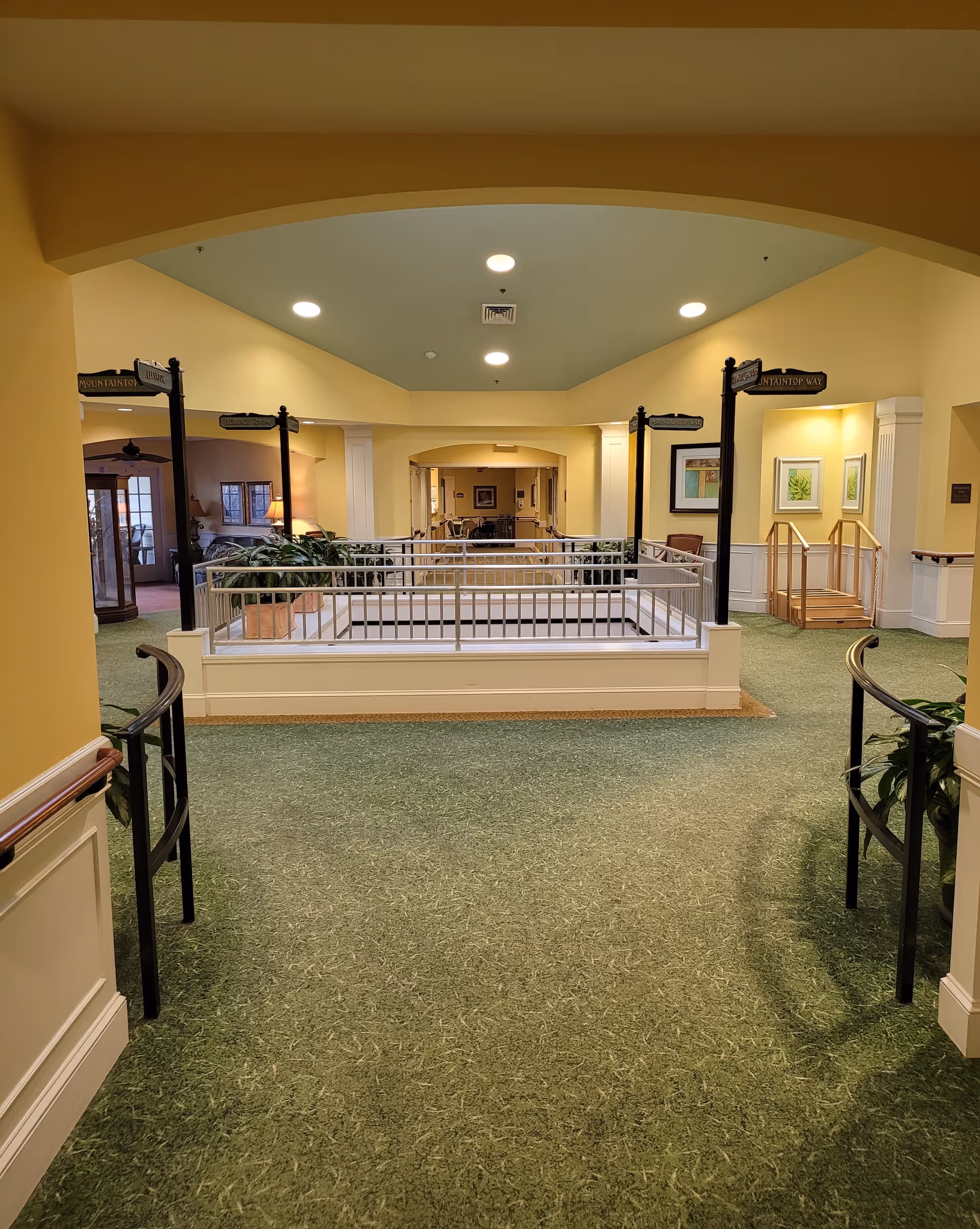 Wide interior corridor with archways, railings, and green carpet in Hillcrest Convalescent Center.