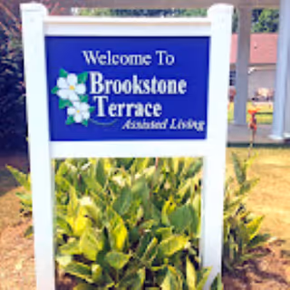 Blue Brookstone Terrace sign welcomes visitors with white posts and plants.