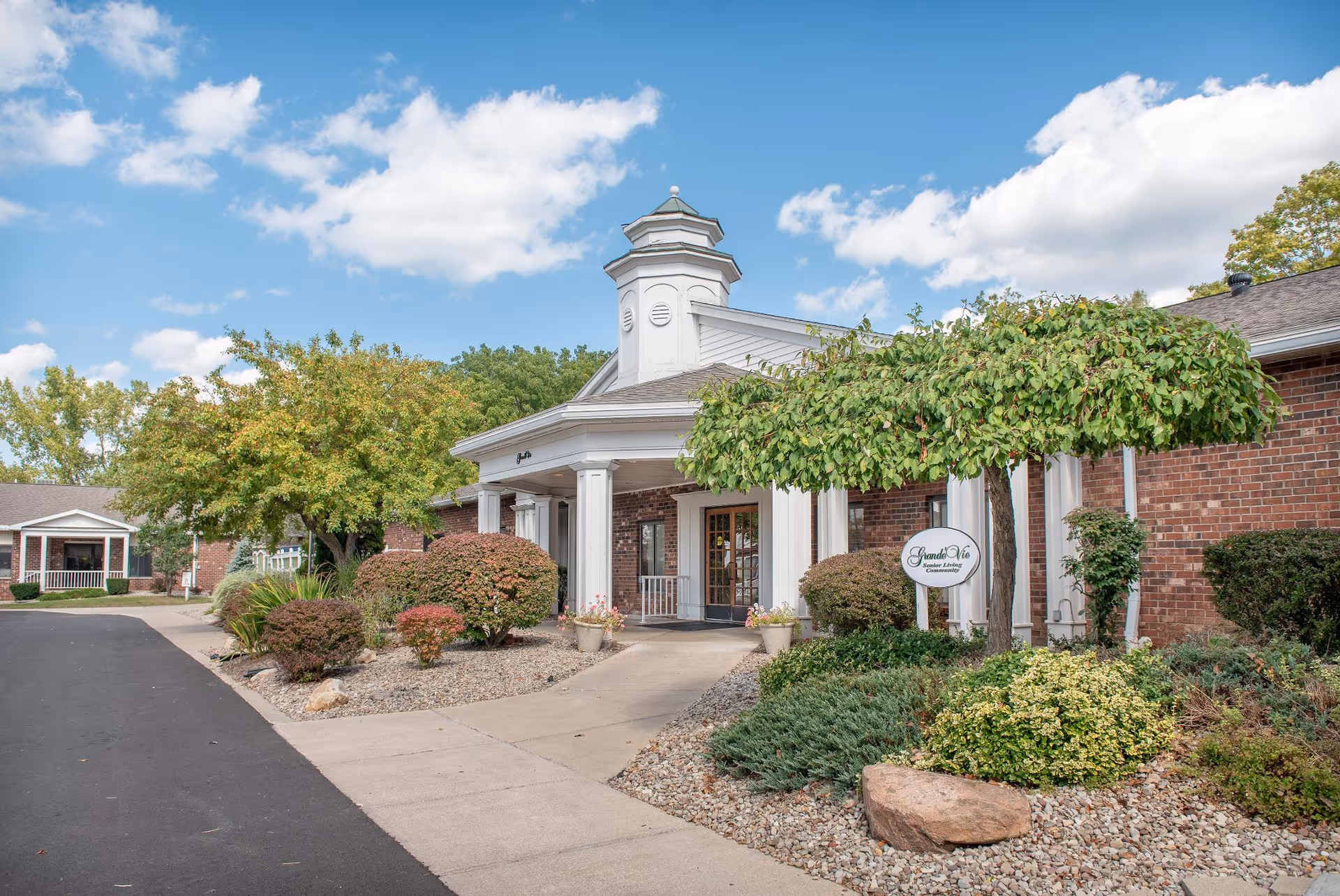 Brick senior living facility with white entrance portico and landscaped shrubs.
