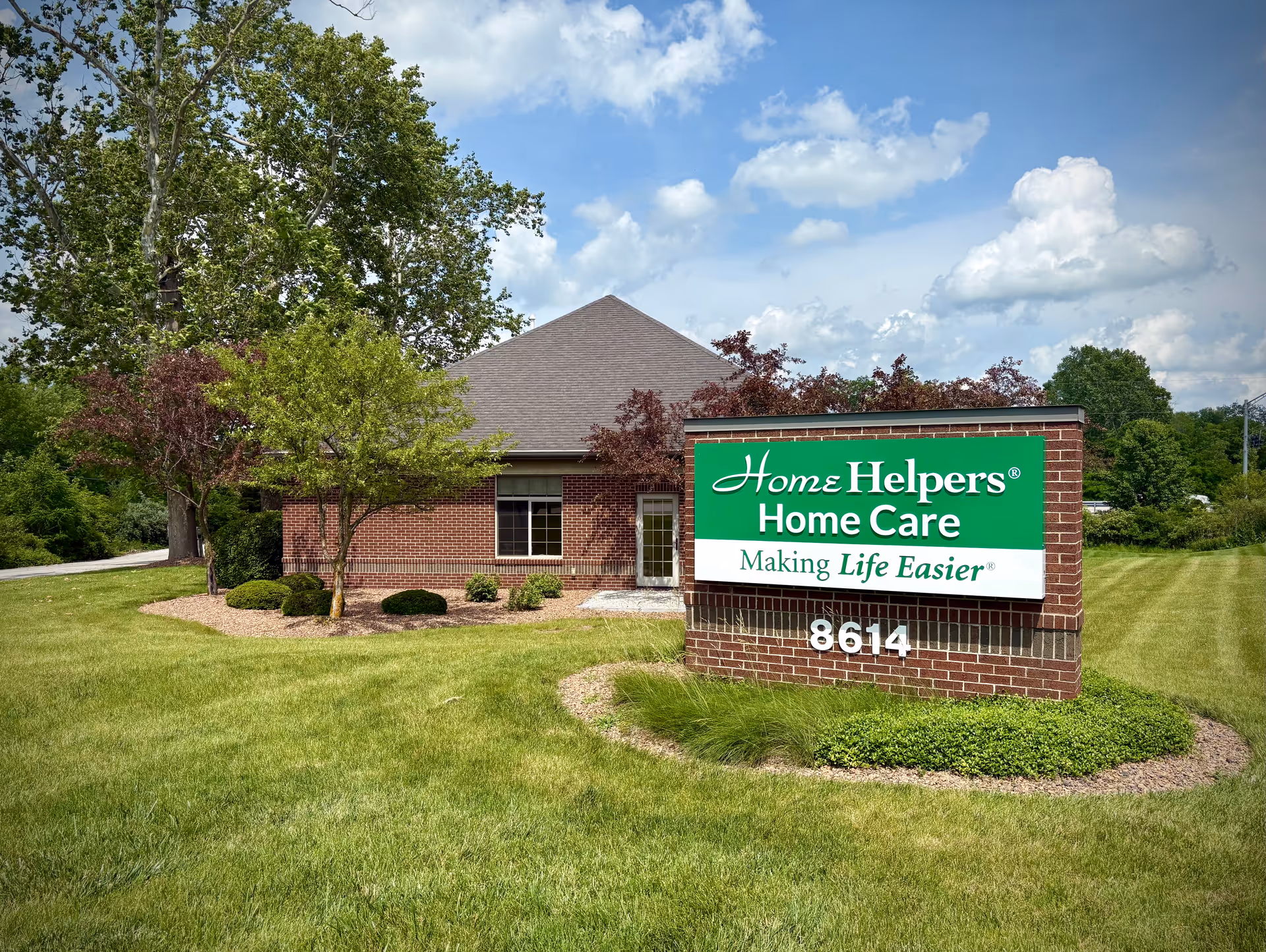 Brick facility with a large green Home Helpers Home Care sign on the lawn.
