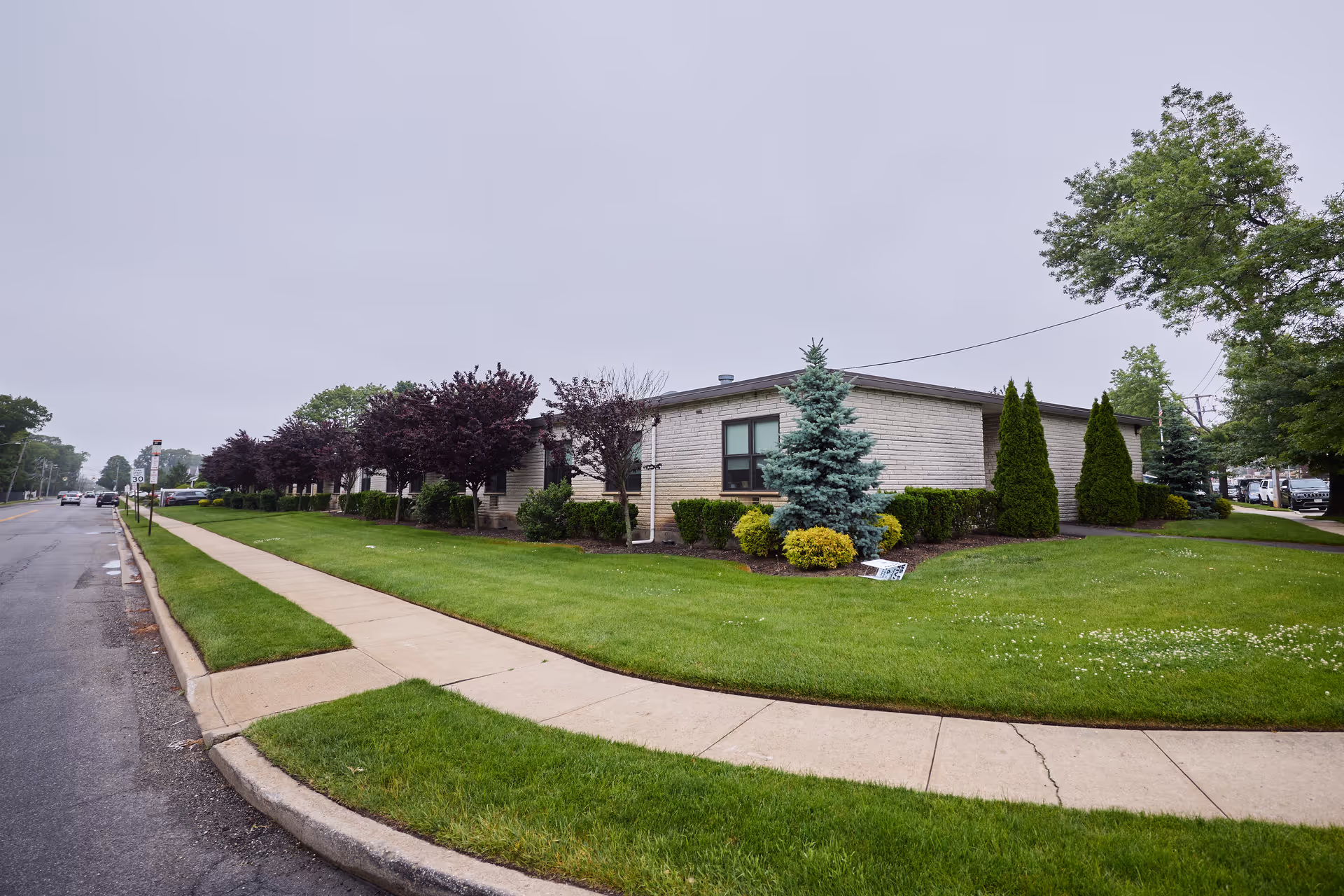 A single-story beige-brick senior living facility with a manicured lawn and curved sidewalk.