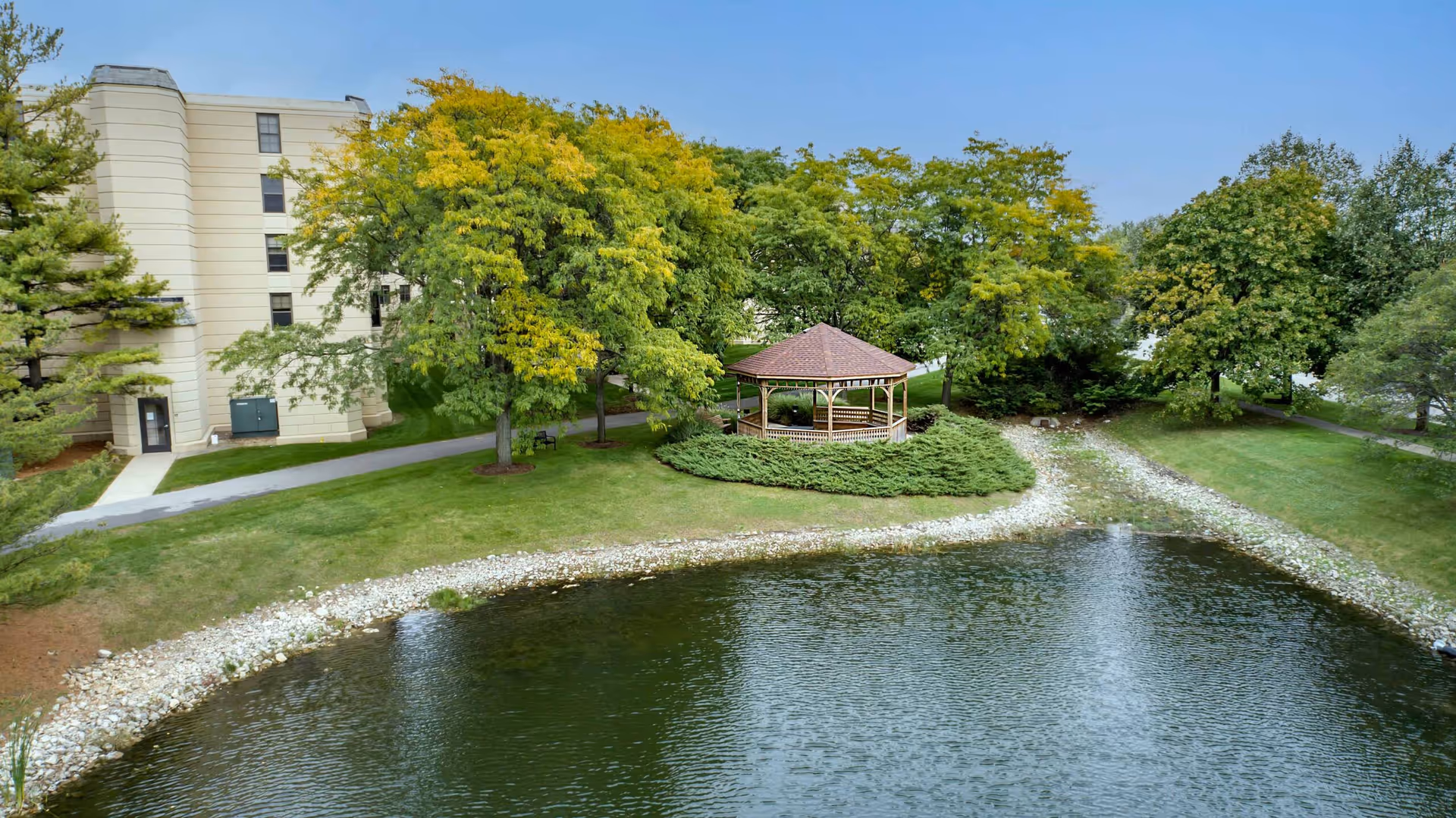 Exterior view of The Commons at Lisle Creek Estates featuring a pond, gazebo, and trees.
