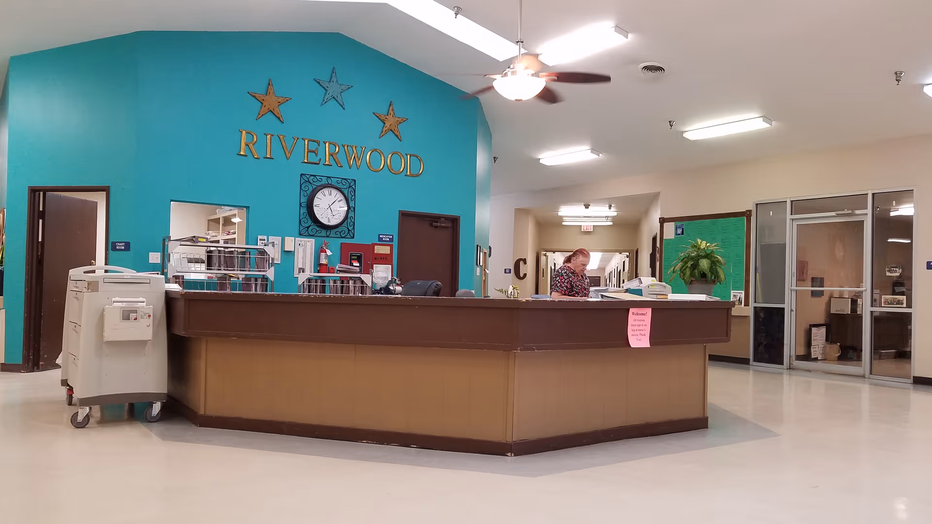 Reception area in Riverwood lobby with teal wall, clock, and staff at desk.
