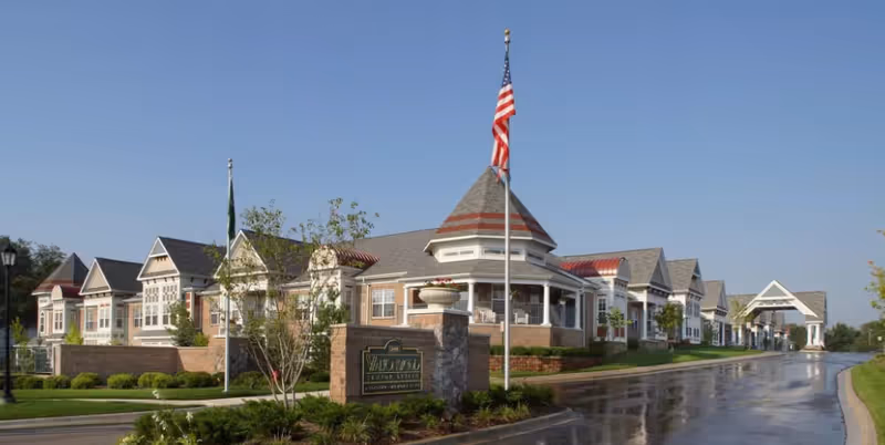 Front exterior of the Waltonwood Main senior living facility with a landscaped driveway, entrance canopy, and an American flag.