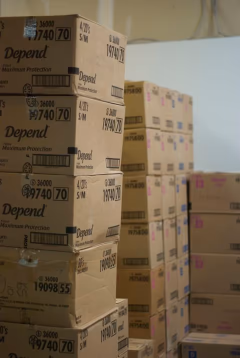 Stacks of cardboard boxes labeled Depend in a storage area for KKMS diaper service.