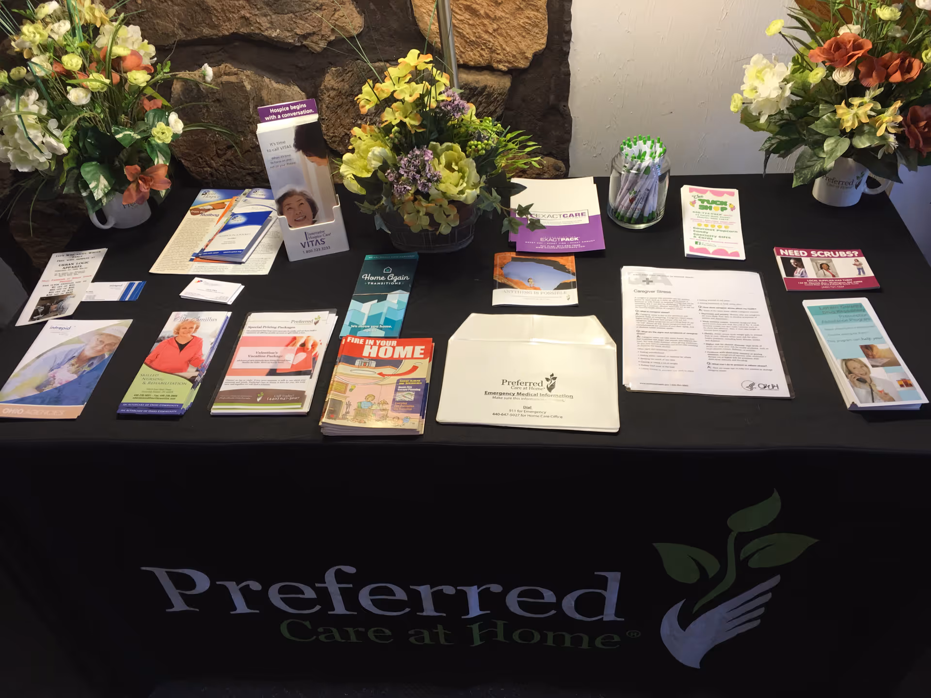 A brochure table for Preferred Care at Home with pamphlets and floral decorations.