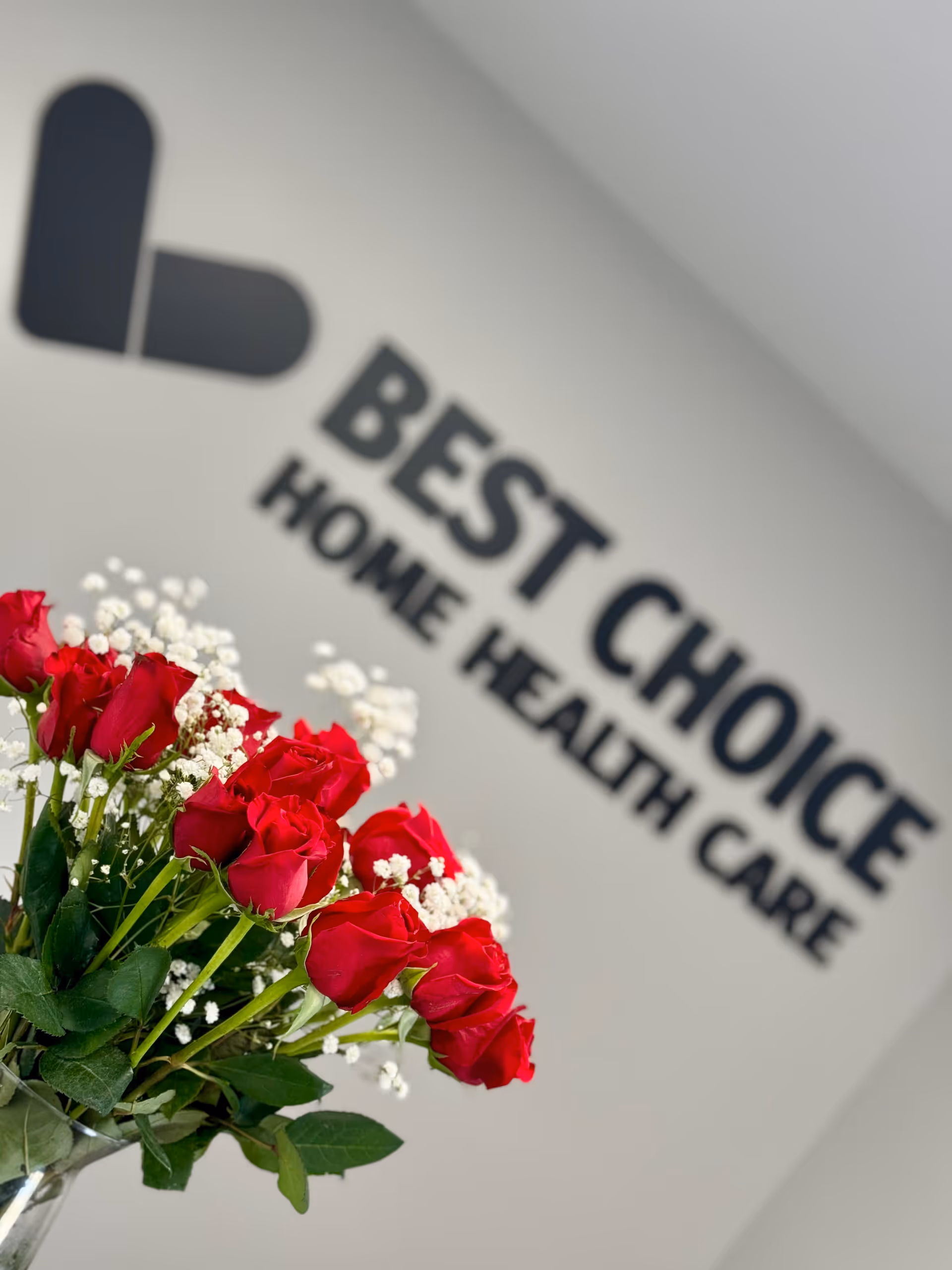 Bouquet of red roses with baby's breath in front of blurred Best Choice Home Health sign.