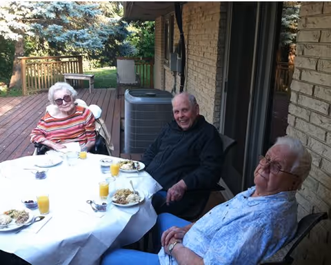 Three elderly residents enjoy a meal outdoors on a deck patio at Grace Homes.