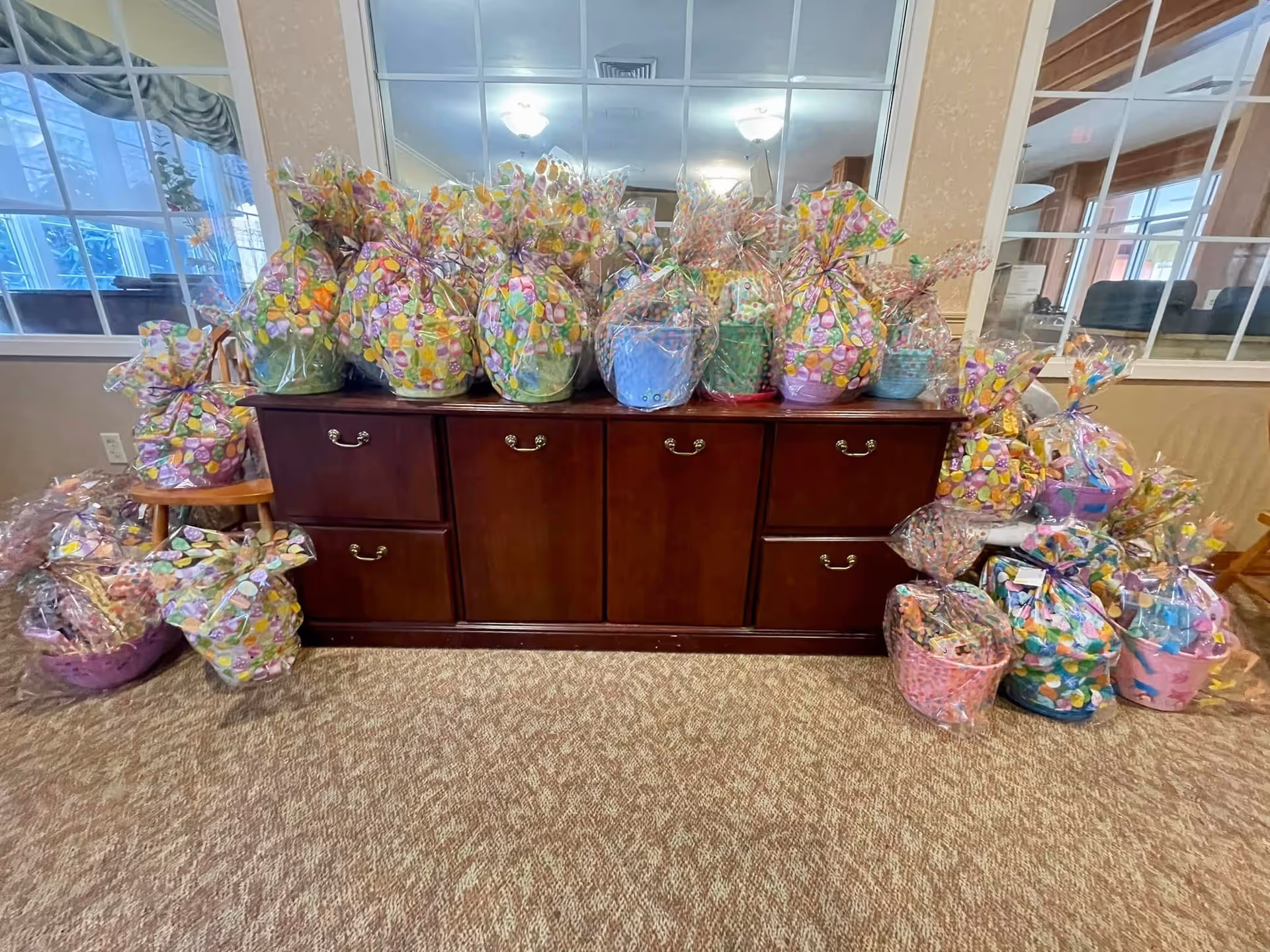 Colorful gift baskets wrapped in cellophane sit atop a wooden cabinet in a bright lobby.