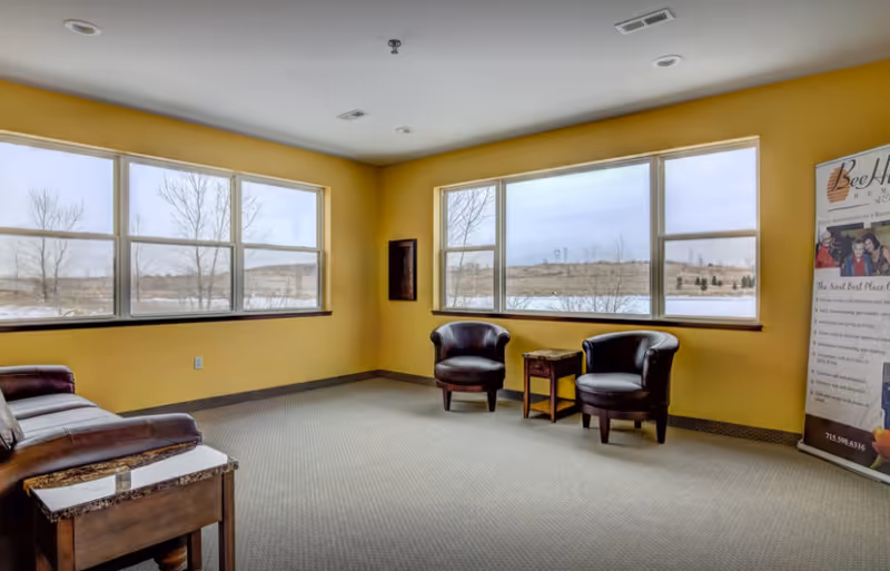 Bright yellow interior lounge with windows, leather chairs, small table, and BeeHive Homes banner.
