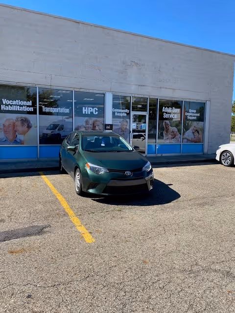 Green car parked outside a storefront with large windows and banners.