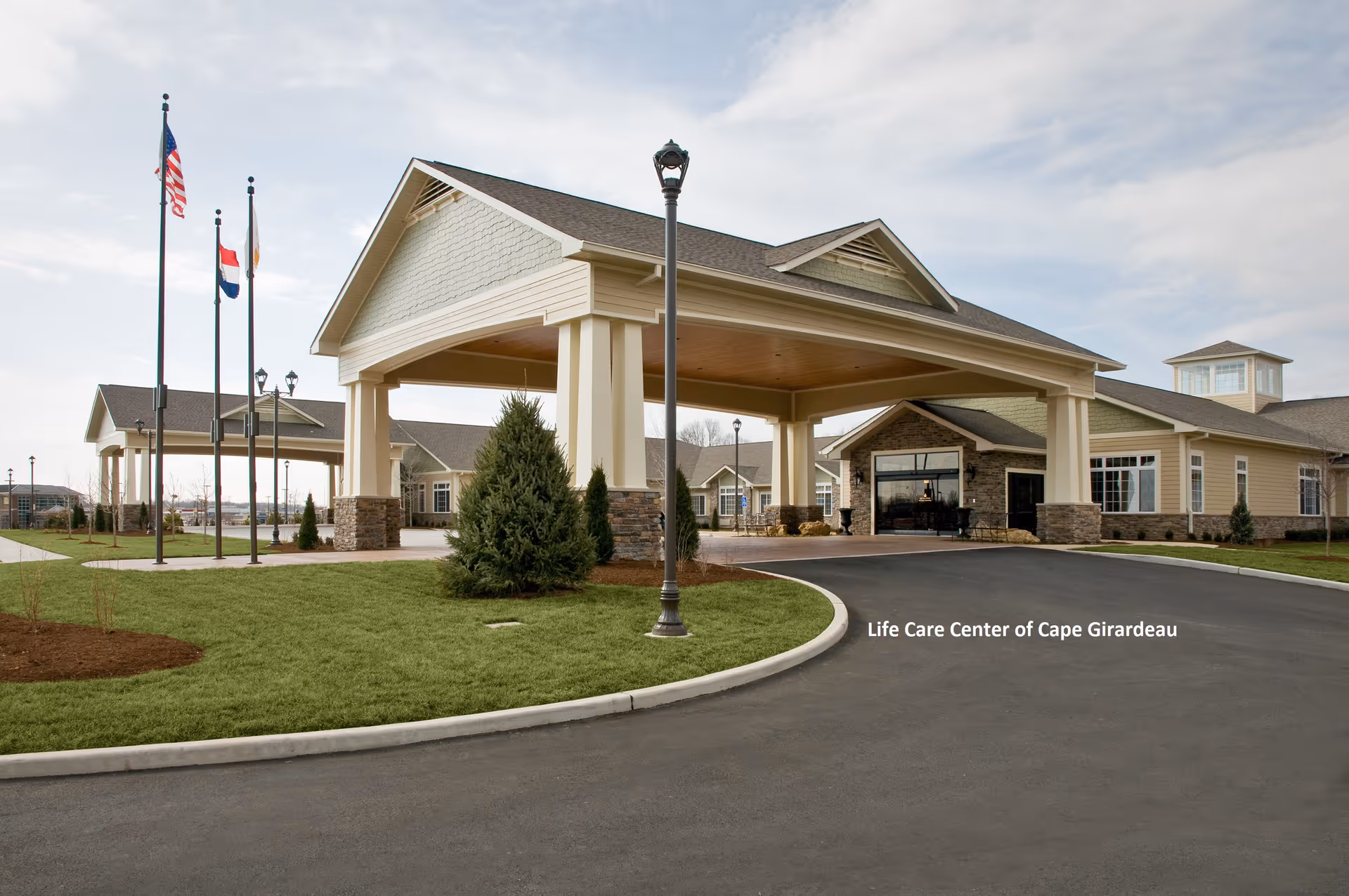 Exterior view of Life Care Center of Cape Girardeau entrance with flags and driveway
