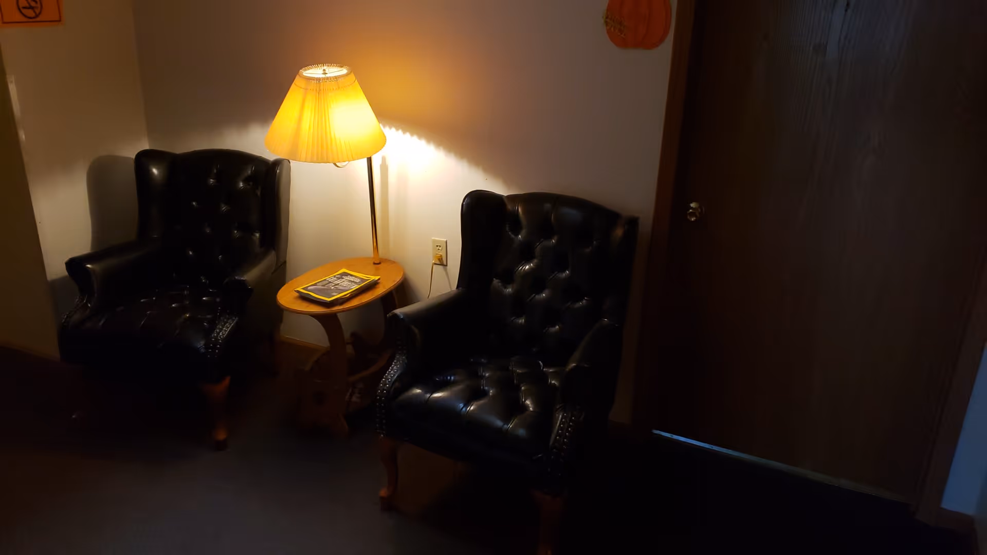 Dimly lit lounge area with two black leather armchairs and a side table with a lamp.
