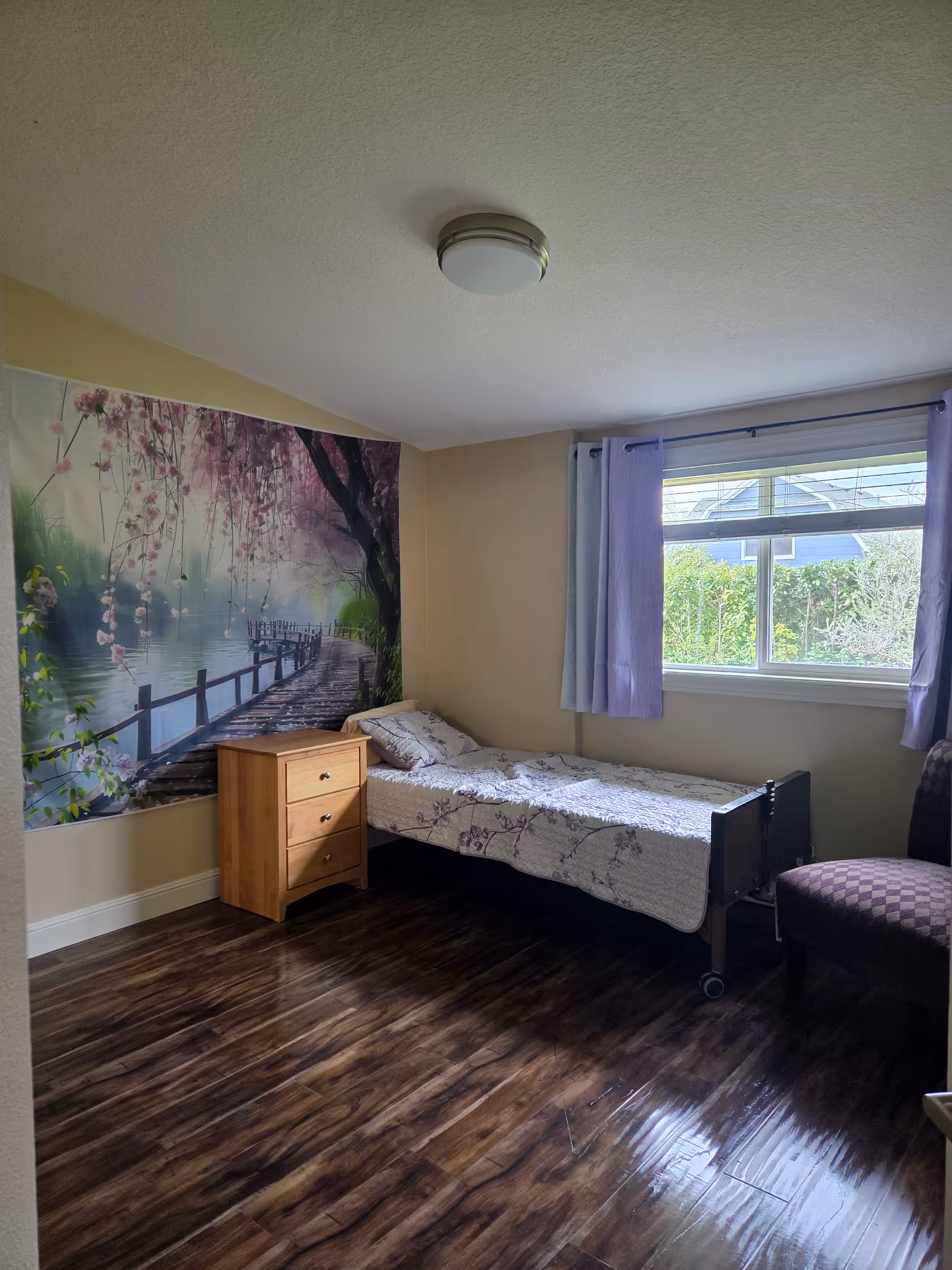 Cozy bedroom featuring a single bed, wooden dresser, wall mural, and a window with purple curtains.