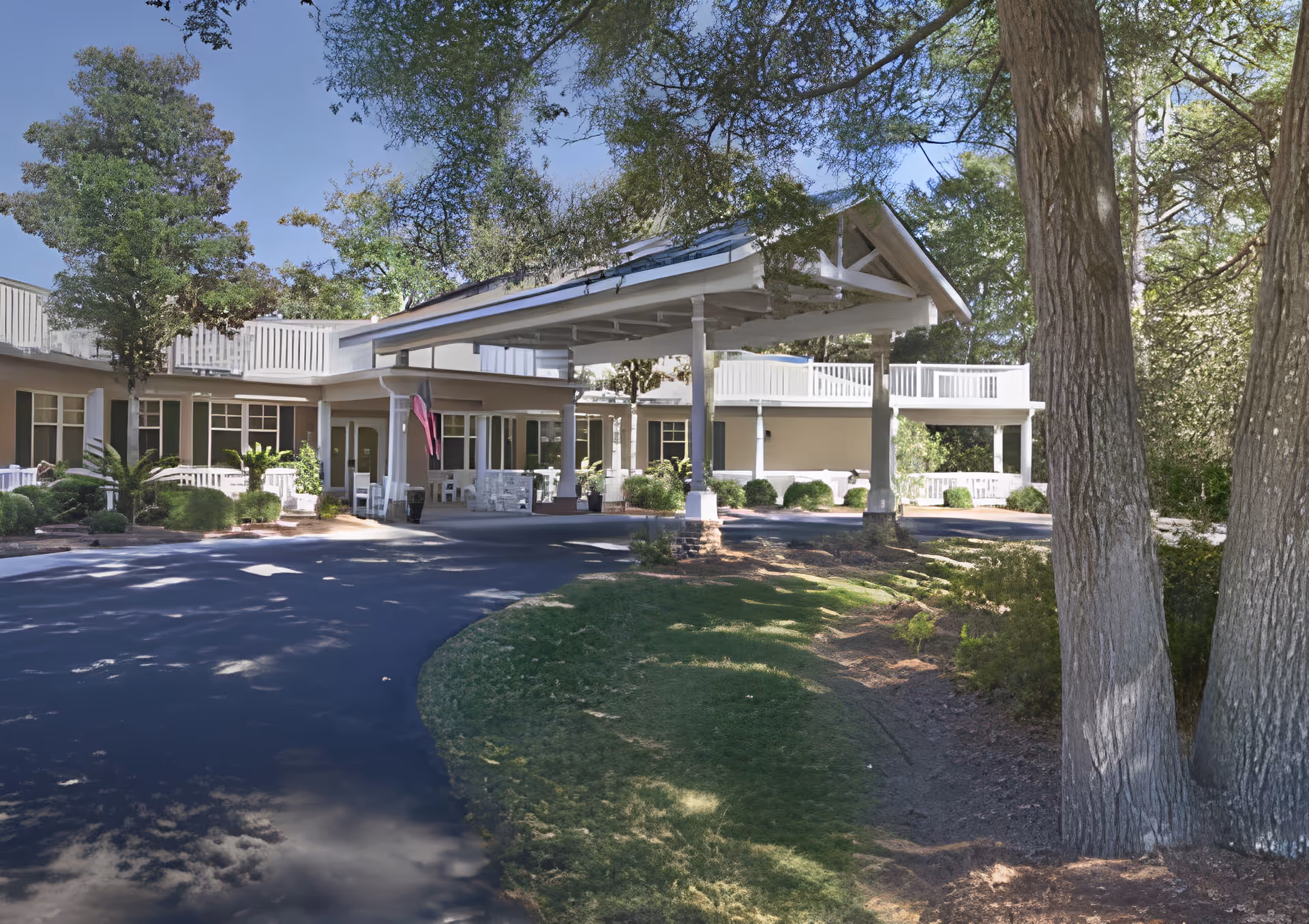 Exterior view of Pines at Hilton Head facility showing a covered entrance with white pillars, surrounded by trees and greenery under a clear blue sky.