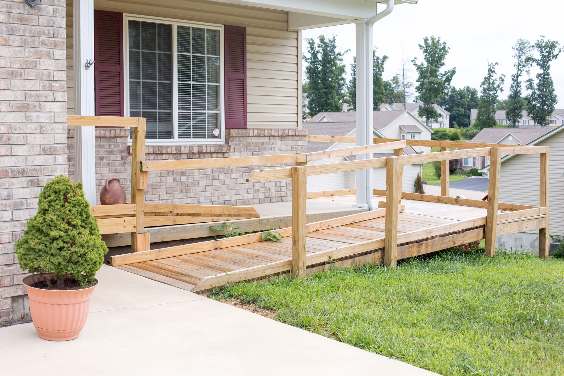 Wooden ramp leads to brick house entrance with a potted plant nearby.
