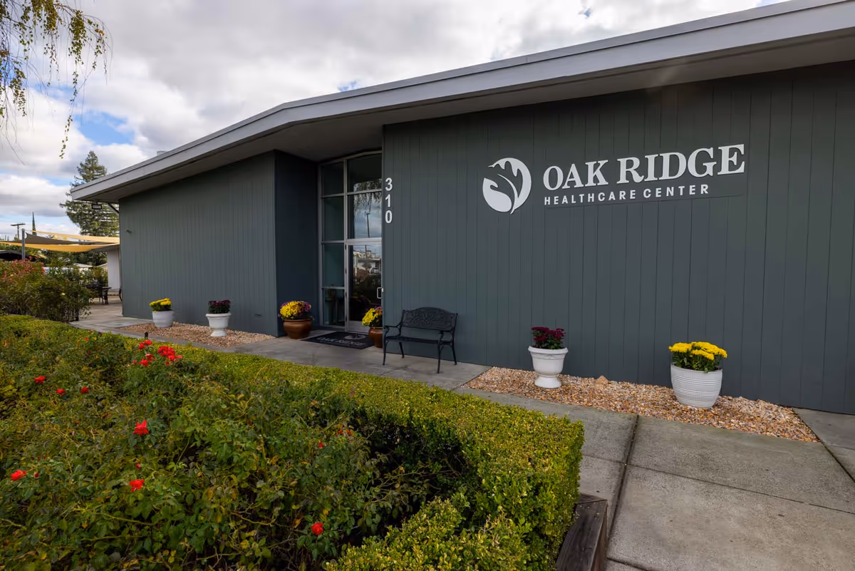 Exterior view of Oak Ridge Healthcare Center entrance with potted flowers and bench.
