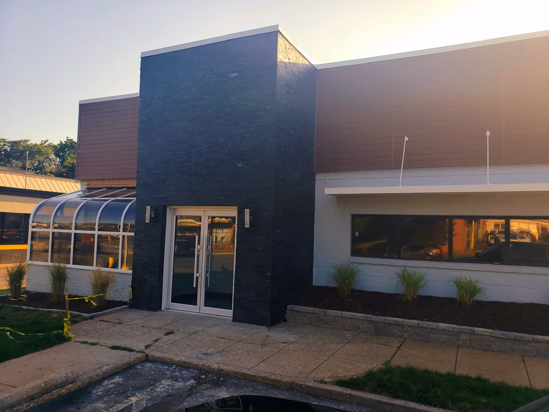 Front entrance of a modern facility with glass doors, dark stone column, and landscaping.
