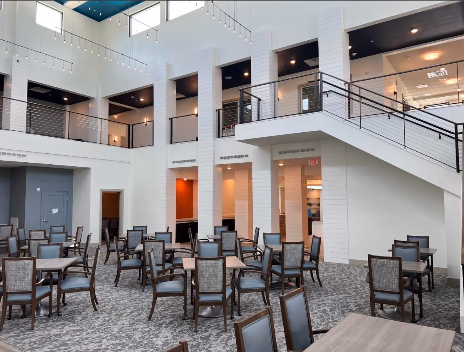 Spacious two-story dining room with multiple tables and chairs, a mezzanine balcony and a staircase.