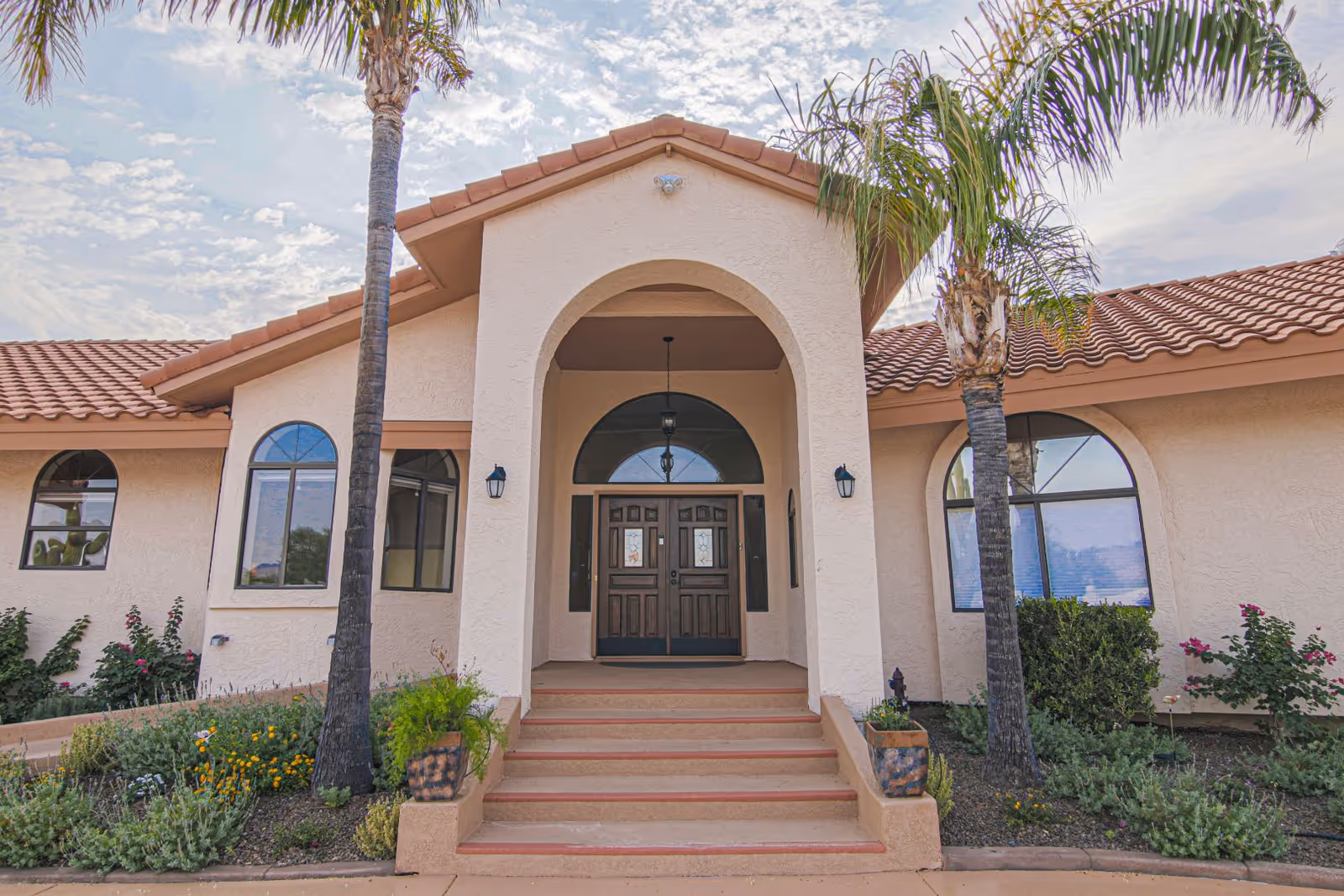 Front entrance of a beige senior living facility with arches and palm trees.