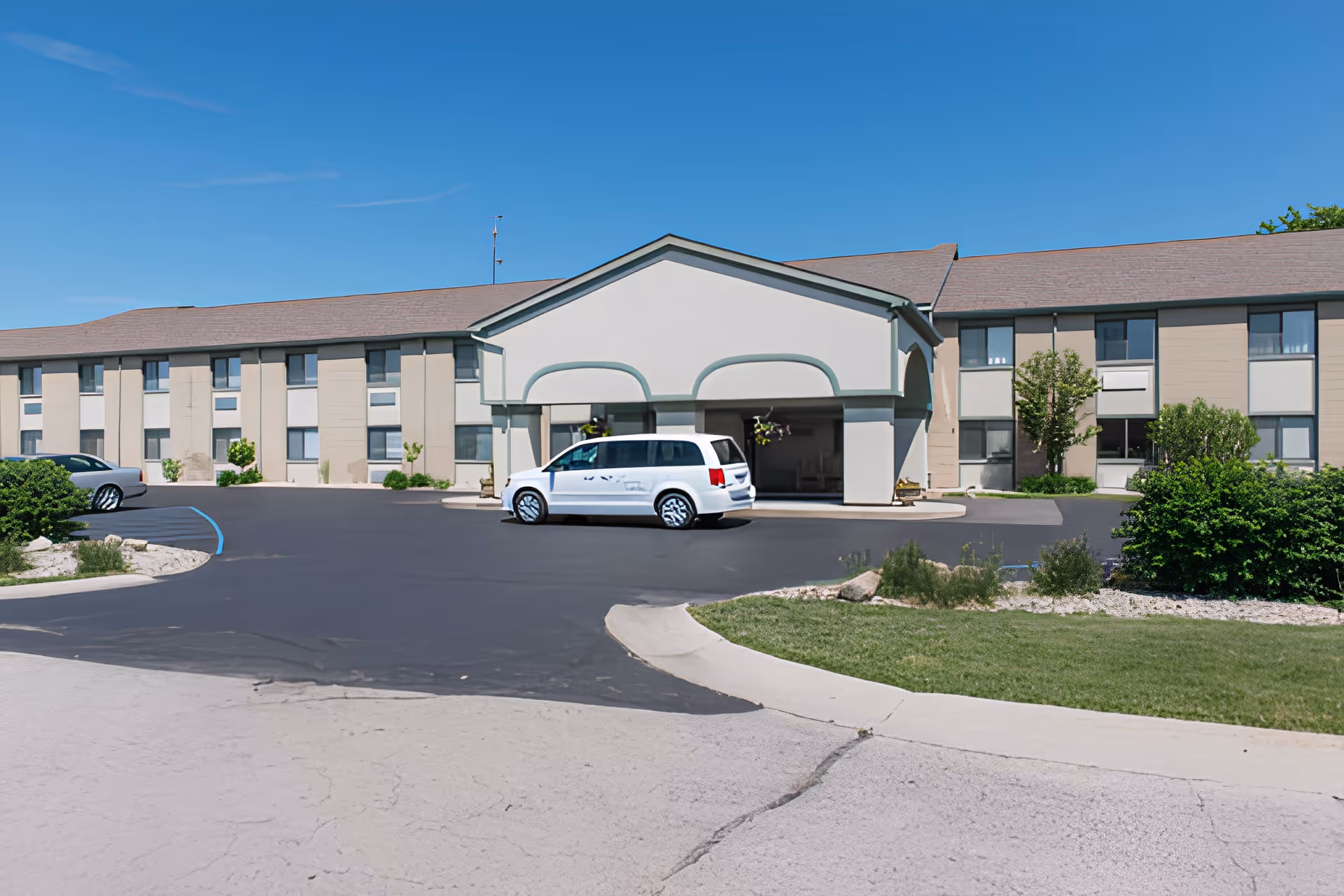 Front entrance of a two-story senior living facility with a covered porte-cochere and a white van parked in the driveway.