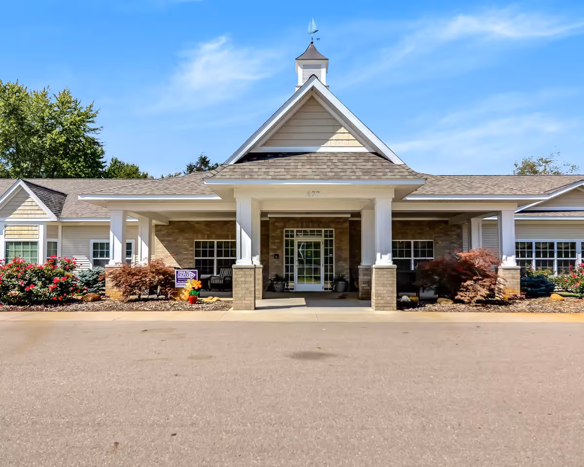 Front view of Maple Lake Assisted Living entrance with columns, brick facade, and landscaped shrubs.