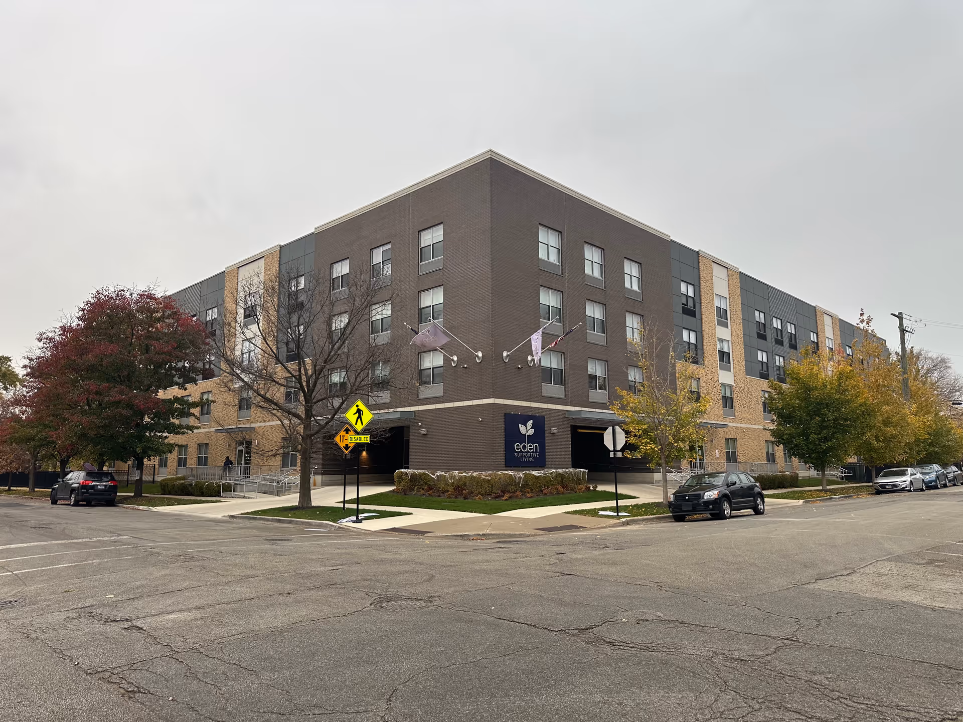 Four-story Eden Supportive Living facility on a street corner with trees and parked cars.