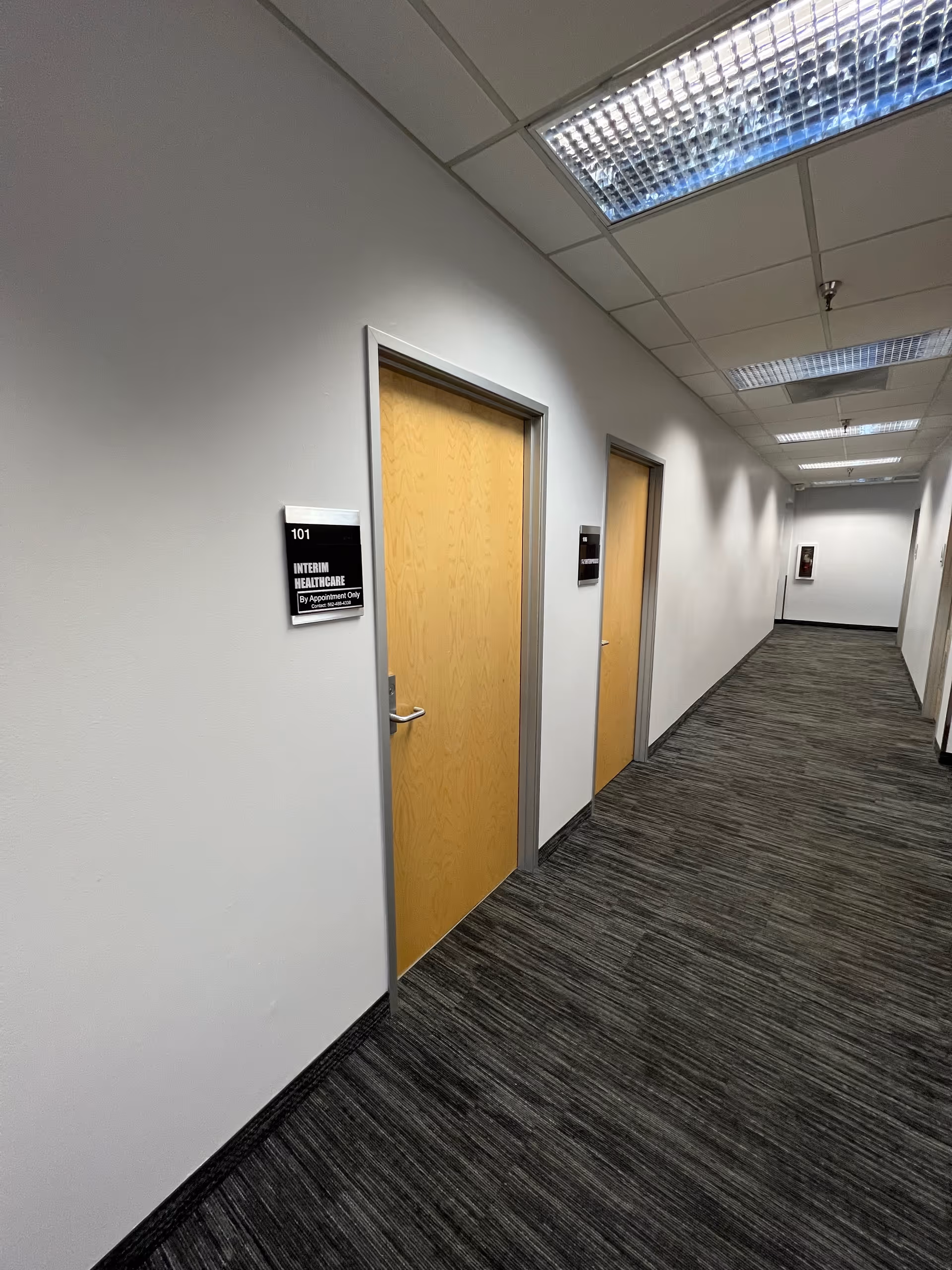 Interior hallway of a facility with wooden doors and room signs.