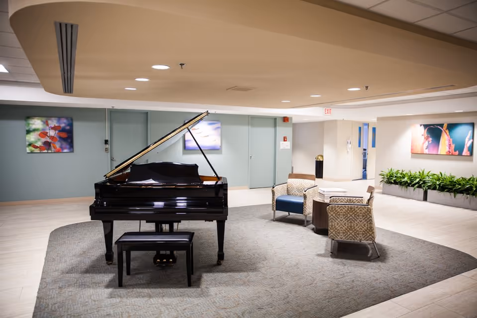 A spacious interior lobby with a black grand piano, a small seating area, artwork on the walls, and potted plants.