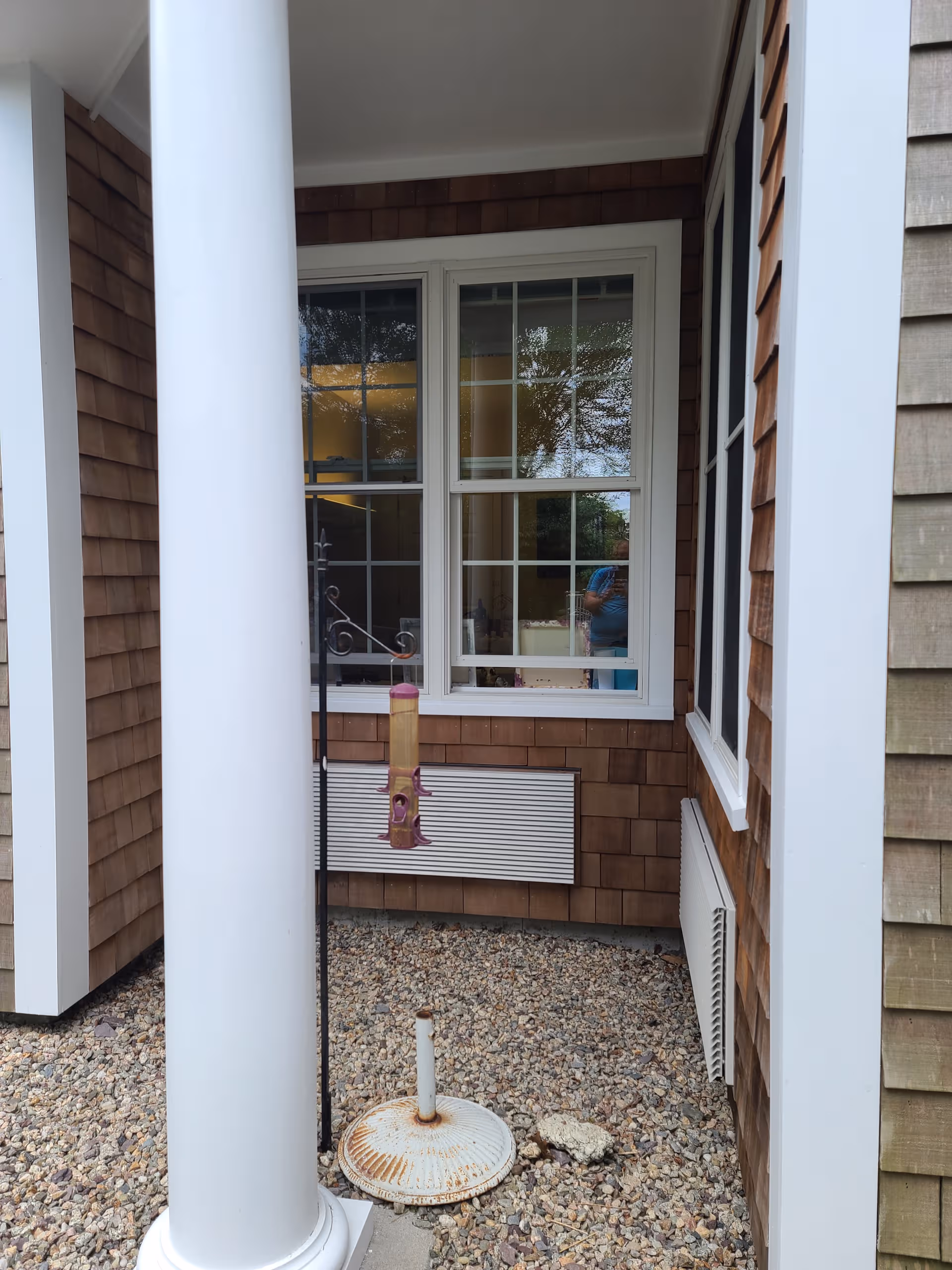 Exterior view of a brown shingle building with white columns and a window.